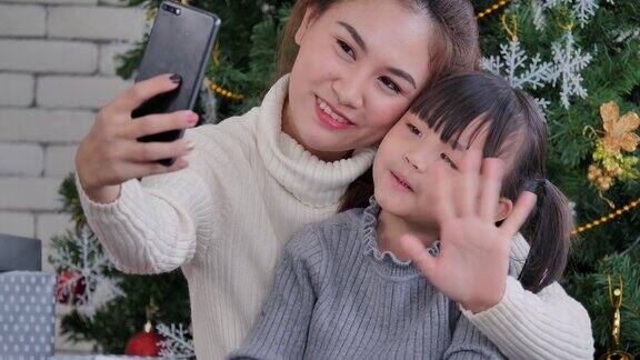 6岁的亚洲母亲和女儿在社交距离中使用智能手机和视频会议技术在家里的客厅视频电话会议社会电话会议