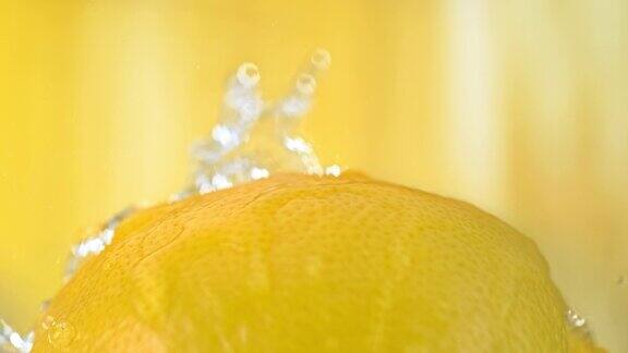 柠檬水果被水泼在黄色背景上的慢动作