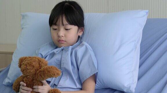 一个中国小女孩躺在医院的病床上抱着一只泰迪熊这个生病的女孩是住院的病人接受了现代化的医疗护理
