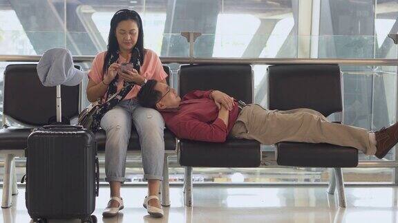 幸福的亚洲老年夫妇坐在候机楼的长椅上用智能手机睡觉等待起飞老年人的旅程老情人旅行飞行退休了在一起假期