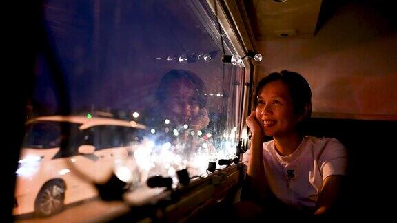一位亚洲妇女坐在露营车的后座上在夜间旅行时透过车窗往外看露营车旅行系列