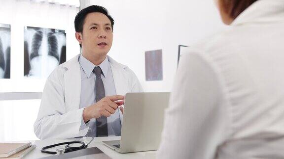 严肃的亚洲男医生正在用笔记本电脑传送好消息谈论结果或症状与女病人坐在医院办公室的桌子前