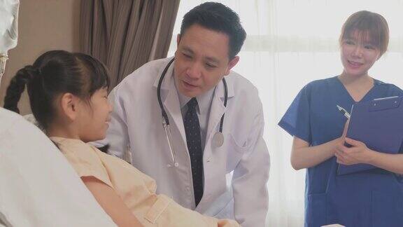 亚洲医生和护士跟踪小女孩病人的症状躺在床上而孩子在医院的康复室专业医生为儿童提供检查和治疗服务