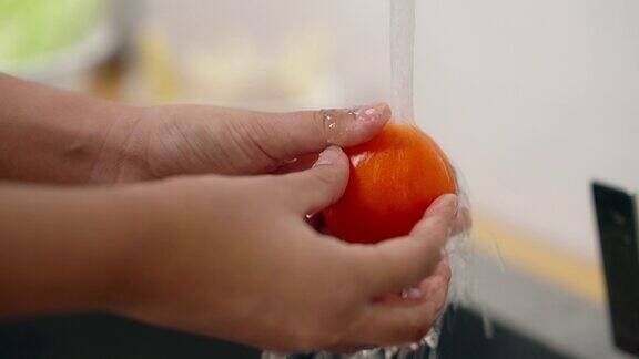 女人的手正在自来水下洗西红柿轻轻地揉搓