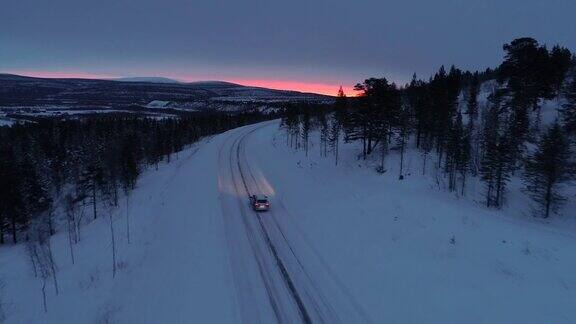 日落时分一辆汽车在雪山公路上穿过松林
