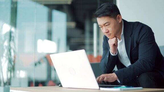 西装革履的亚洲商人在现代办公中心用笔记本电脑办公自信认真的男性经理员工满意愉快忙发短信