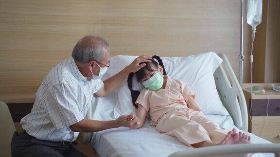 亚洲小女孩戴着口罩躺在康复室的床上父亲来到康复室探望并照顾她的女儿