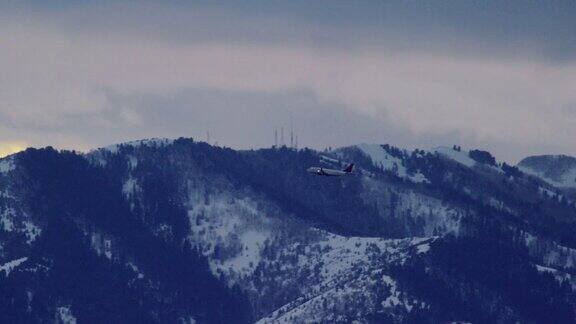 冬季日落日出时一架商业客机飞过犹他州积雪覆盖的山脉