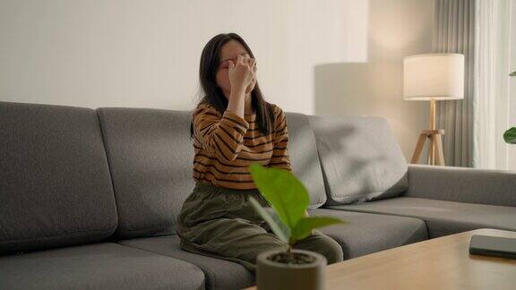一名使用智能手机的亚洲妇女坐在家里的沙发上眼睛疼