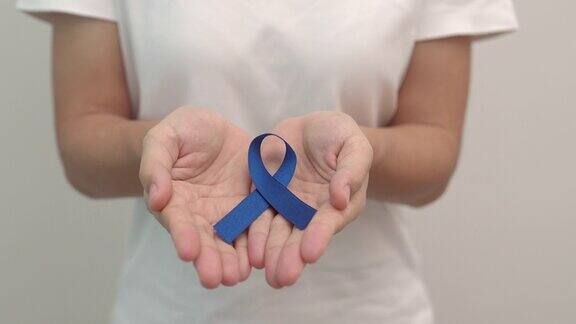 3月大肠癌宣传月妇女手持深蓝色丝带支持生活和疾病的人保健、希望和世界癌症日