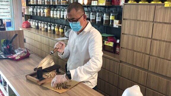 亚洲华裔男性药剂师在中药店柜台前切中药