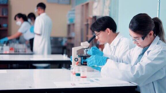 不同的工业科学家和工程师团队穿着白大褂在研究实验室用显微镜工作