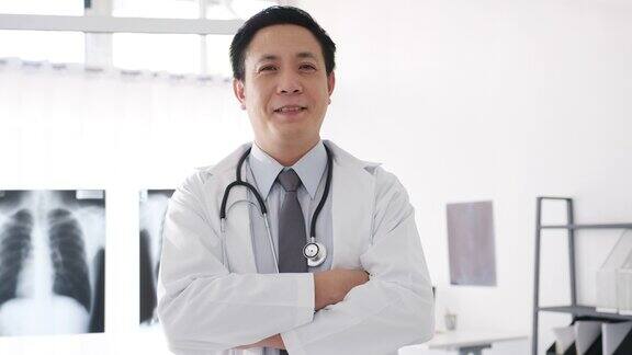 年轻的亚洲男医生在白色医疗制服听诊器看着相机微笑和双臂交叉而与病人在健康医院的视频电话会议