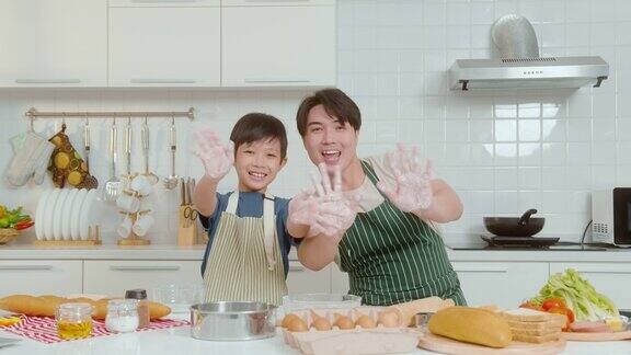 快乐微笑的年轻亚洲父亲和儿子在家里的厨房做饭