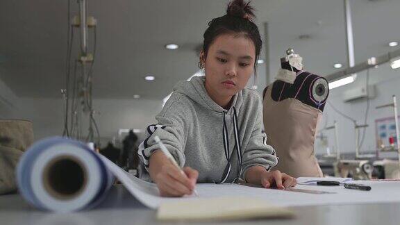 亚洲华裔女时装大学生在学院车间做服装项目写下尺寸画出缝纫图案