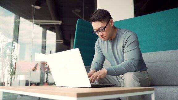 肖像有思想的年轻亚洲自由职业者在现代办公桌上用笔记本电脑工作自信专注沉思的男士室内企业家