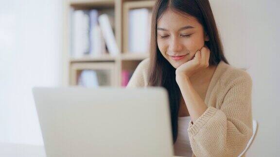 年轻的亚洲女性在家工作快乐的女性在家里的桌子上使用笔记本电脑