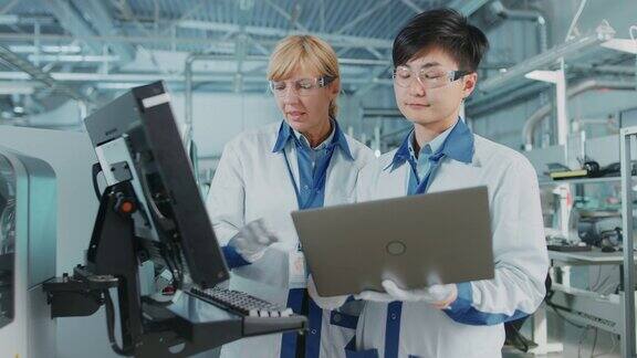 在高科技工厂亚洲工程师与女主管谈话用电脑编程印刷线路板表面贴装装配线的取放电子机械使用SMT设备生产PCB