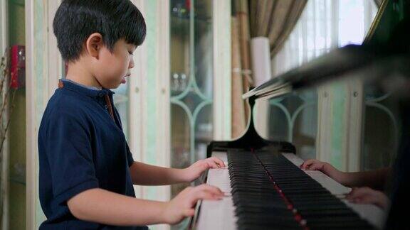 侧视亚洲男孩在客厅里弹钢琴有选择性的重点孩子专心上课业余爱好和在家学习快乐的一天和家庭活动和生活方式