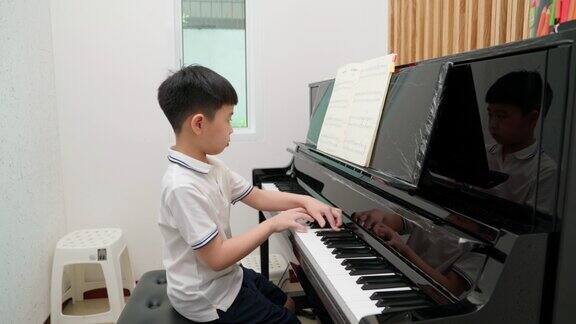 一个亚洲男孩在学校的教室里穿着衬衫弹钢琴考试要上一级教育、技能、学习理念音乐家钢琴练习网络考试新常态