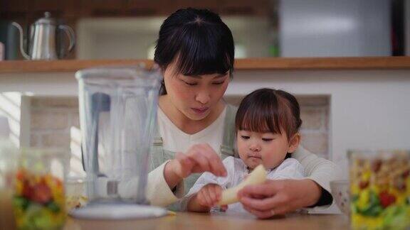 妈妈帮助她的小女儿做奶昔并鼓励她健康饮食
