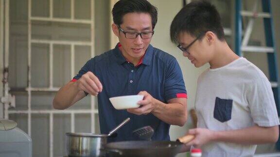 周末一位亚洲华人父亲在自家后院的厨房教儿子做饭准备晚餐