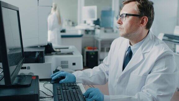 男性研究科学家坐在他的工作场所在实验室使用个人电脑背景遗传学、药学研究中心配备创新设备