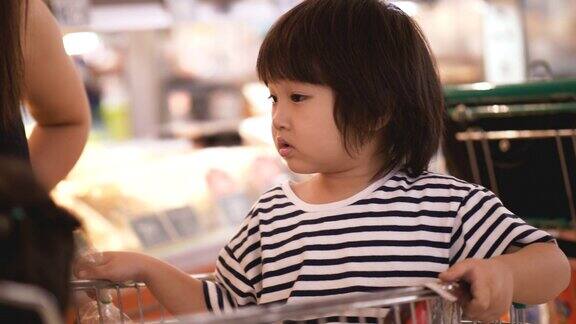 亚洲家庭由男孩和女孩在购物车上他们的父母在杂货店购物
