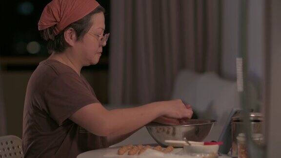 亚洲华人中成年妇女在家里的厨房里双手将花生饼干面团压在手掌上成型