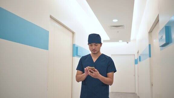 亚裔华人男外科医生在医院走廊上用手机发短信