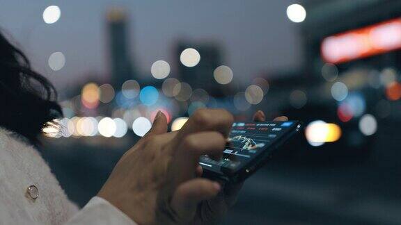 女性手握着手机在城市街道上浏览互联网的特写与模糊的灯光在夜晚