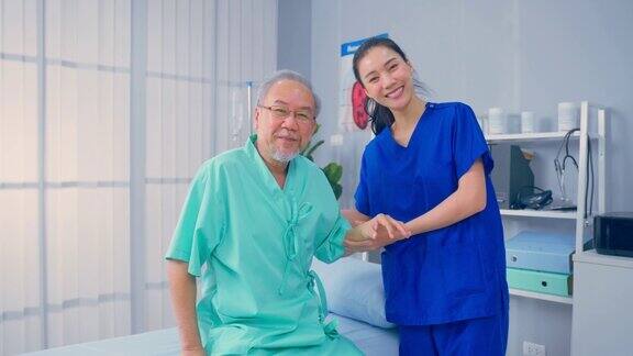 肖像的亚洲女性治疗师和资深男性患者在医院有吸引力的女性专科医生做物理治疗程序的老年成熟的男性然后看相机在预约期间