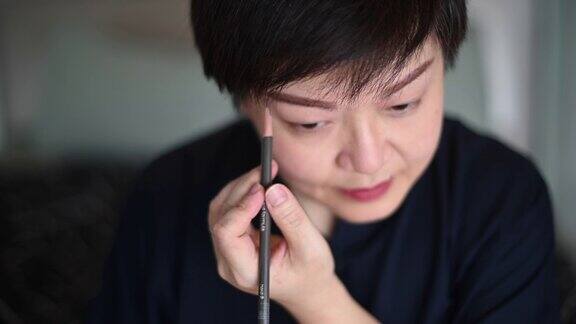 一位亚洲华人中年人正准备在离开她的公寓或画眉毛之前化妆