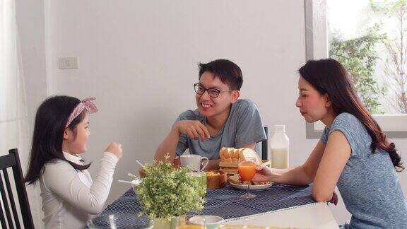日本亚裔家庭在家里吃早餐亚洲的妈妈爸爸和女儿感到愉快的谈话在一起吃面包玉米片谷物和牛奶碗在厨房的桌子上在早上