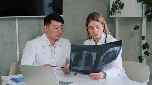 两个不同的医生交谈和使用笔记本电脑分析病人的x光片谈结果分析医疗保健诊所亚洲主任外科医生和放射科医生讨论咨询病人的肺部图像