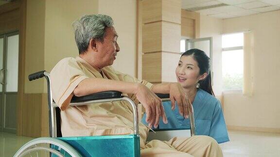 在医院照顾坐在轮椅上的成熟男性病人的亚洲护士年轻女子与老人交谈并照顾手术后恢复的老年病人女孩对老人微笑