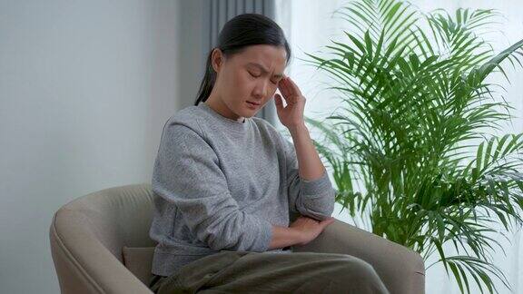 一位亚洲妇女坐在家里客厅的扶手椅上患了头痛