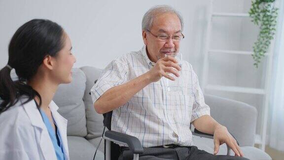 亚洲护工为坐在轮椅上的老年男性提供水迷人的年轻专家护理员女医生支持和照顾快乐的老人成熟的爷爷在养老院