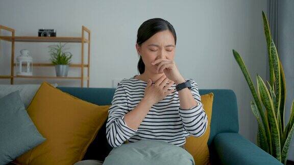 一名亚洲妇女发烧流鼻涕鼻塞和喉咙痛坐在家里客厅的沙发上