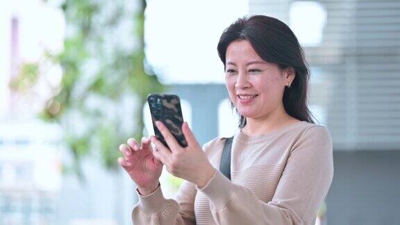 亚洲华人中年妇女在城市街道上使用智能手机微笑