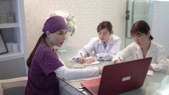 亚洲华人女医生和护士使用笔记本电脑在医生办公室讨论