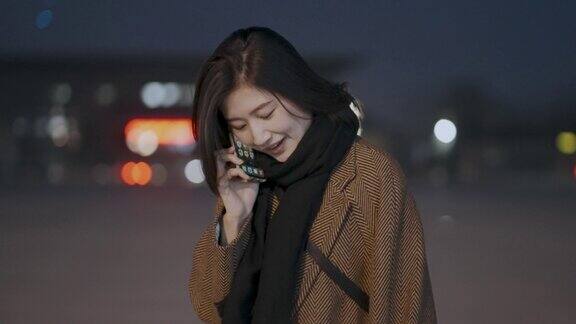 一个年轻漂亮的亚洲女人在夜晚用手机背景是模糊的霓虹灯4k