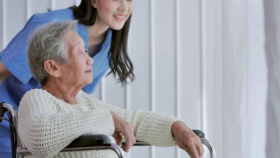 坐在轮椅上的亚洲老年妇女和亚洲年轻女护士医生在靠近窗户在家里或医院交谈老祖母倾听照顾者给予的支持老年人保健家庭保健残疾人