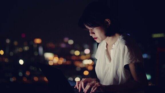 年轻的亚洲女人坐在阳台上用笔记本电脑工作