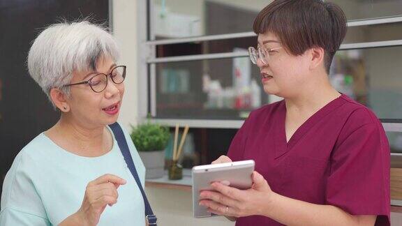 亚裔中国女护士在诊所用数码平板电脑向她的女病人解释体检报告