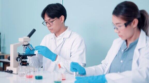 不同的工业科学家和工程师团队穿着白大褂在研究实验室用显微镜工作
