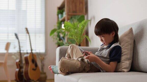 开朗的男孩白天躺在家里的沙发上玩数码平板电脑