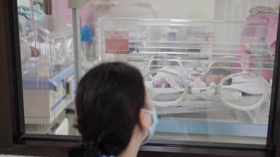 在医院里妈妈细心地看着保温箱里的婴儿