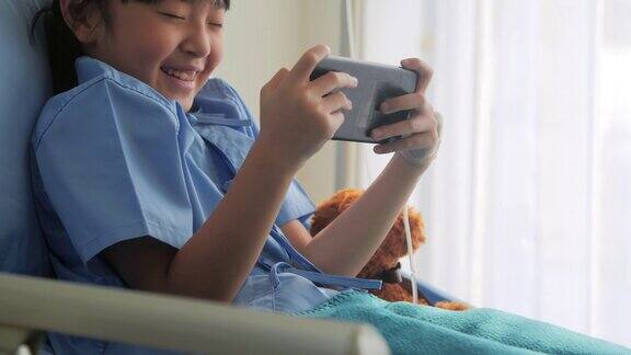 可爱的小女孩躺在儿童医院的病床上在手机上看搞笑的动画片、电影中国和香港的医疗系统