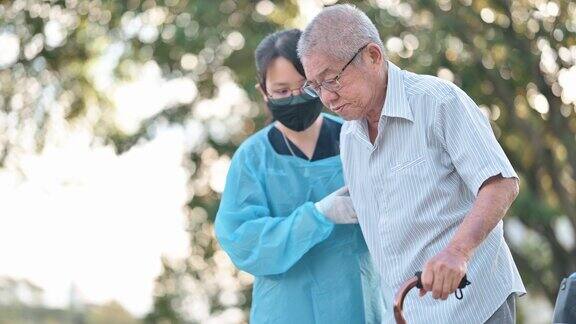 亚裔中国女性理疗师帮助老人拄着拐杖在公园散步